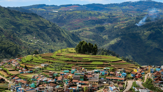 Panoramic view of terraced hills with a densely packed village in the foreground, set against layered mountain ranges in Kodaikanal, Tamil Nadu.