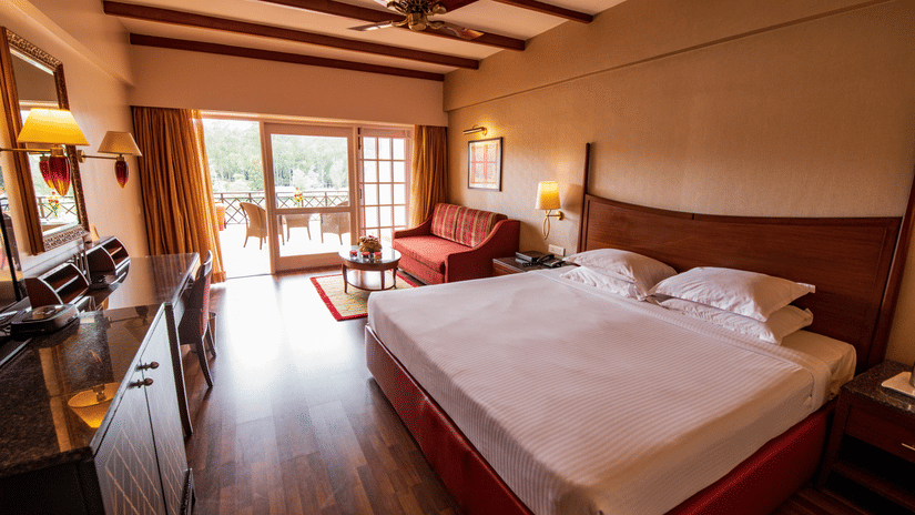 An image of a bedroom featuring a double size bed, a sofa , work desk and chair, and a cabinet table  at The Carlton, Kodaikanal