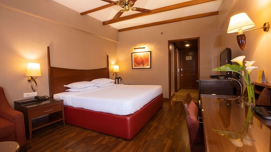 An image of a bedroom featuring  a double size bed, a bedside table, a sofa, and a cabinet table at The Carlton