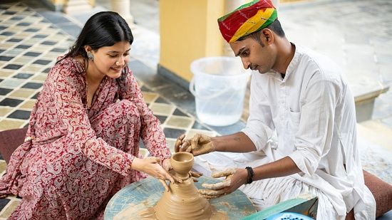 Two people making pottery, with one teaching the other
