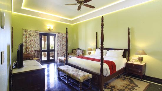 Spacious deluxe room at Juna Mahal featuring a traditional four poster bed, warm lighting and elegant interiors with heritage design elements