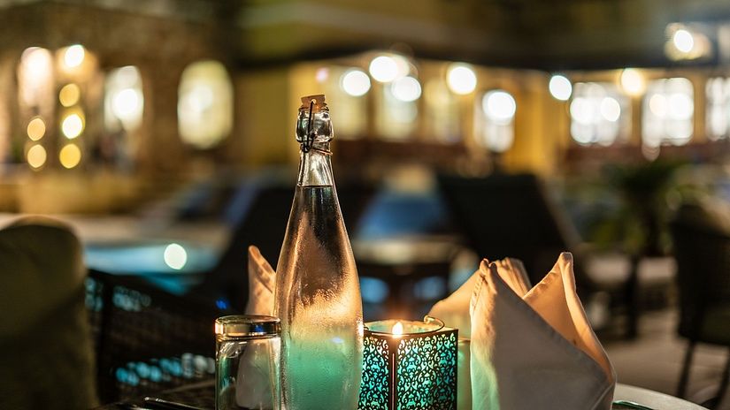 A candlelight dinner table set with a lit candle, tissues, and a glass bottle