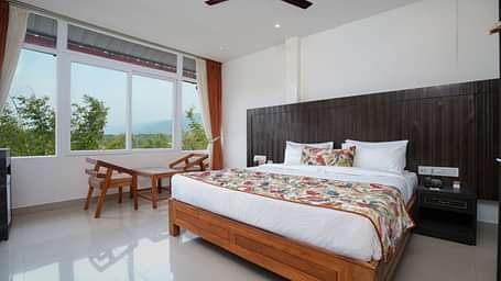 Deluxe room featuring large windows with a nature view, a spacious bed, air conditioning, wooden storage units, and a television at Summit Green Lake Tea Resort & Spa, Kaziranga4