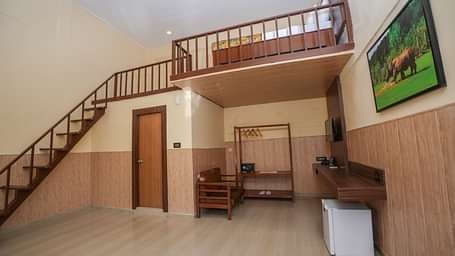 Duplex room with balcony features a living area with wooden furniture, a wine fridge, wall-mounted television, and stairs leading to the spacious bedroom at Summit Green Lake Tea Resort & Spa, Kaziranga