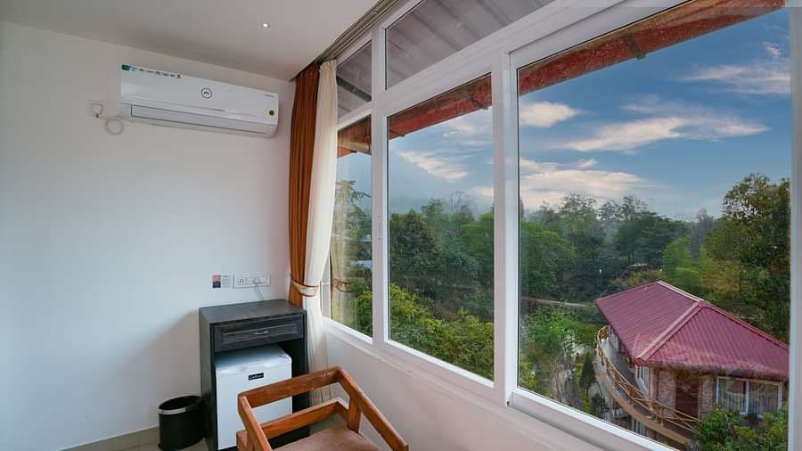 Deluxe room featuring large windows with a nature view, a spacious bed, air conditioning, wooden storage units, and a television at Summit Green Lake Tea Resort & Spa, Kaziranga1
