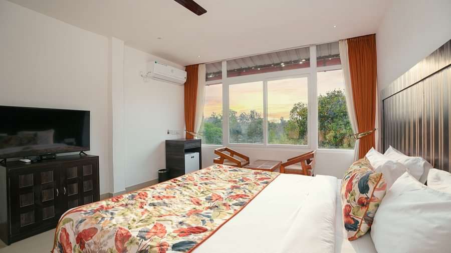 Deluxe room featuring large windows with a nature view, a spacious bed, air conditioning, wooden storage units, and a television at Summit Green Lake Tea Resort & Spa, Kaziranga2