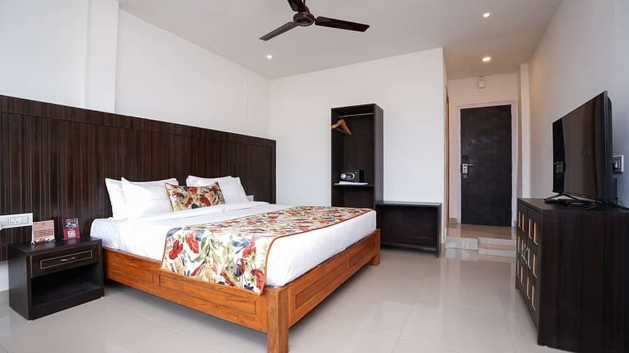 Deluxe room featuring large windows with a nature view, a spacious bed, air conditioning, wooden storage units, and a television at Summit Green Lake Tea Resort & Spa, Kaziranga6