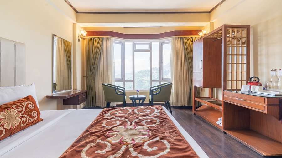 king size bed and chairs in the background near balcony of premium room at Summit Lillium Hotel & Spa, Kalimpong