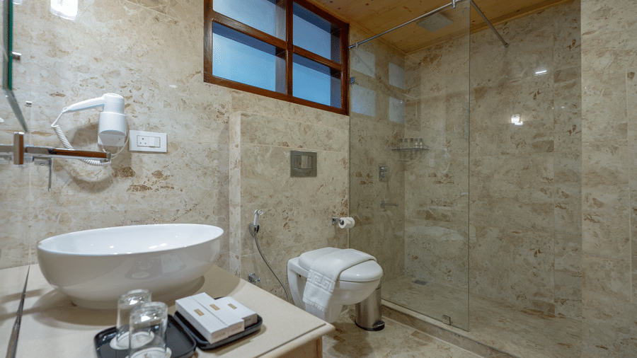 A bathroom at Summit Norbu Ghang - The Signature Collection, Gangtok, with sink, mirror, glass shower enclosure, and tiled walls.