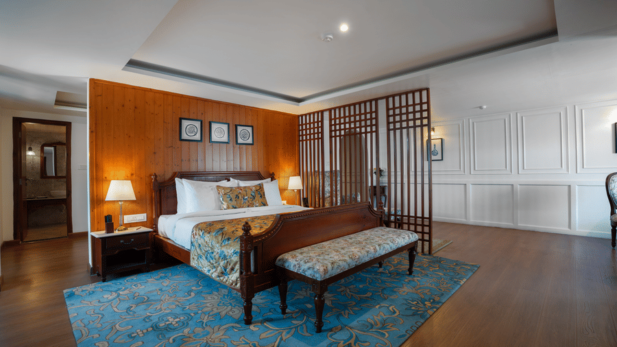 A bedroom at Summit Norbu Ghang - The Signature Collection, Gangtok, with a king size bed, bench, lamps, wardrobe panels, and carpeted floor.