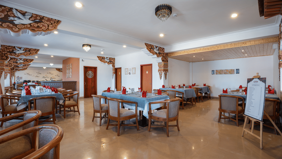 The dining hall at Summit Norbu Ghang - The Signature Collection, Gangtok, with arranged tables, wooden chairs, and ceiling decor.
