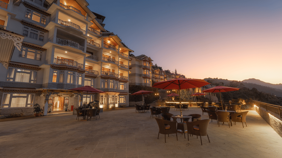 The facade view of Summit Norbu Ghang - The Signature Collection, Gangtok, with multi-storey building, outdoor seating, and evening sky.