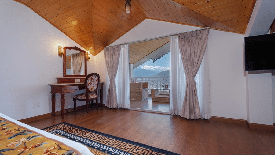 A suite at Summit Norbu Ghang - The Signature Collection, Gangtok, with a king size bed, desk, balcony doors, wall-mounted TV, and vanity.