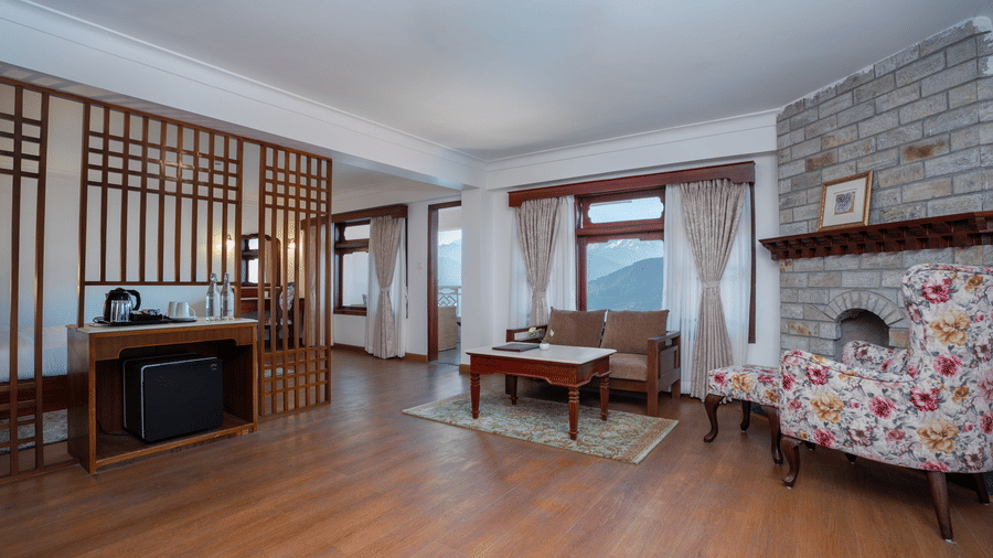 A bedroom interior at Summit Norbu Ghang - The Signature Collection, Gangtok, with a sofa, armchair, teapoy, stand table, windows, and fireplace wall.