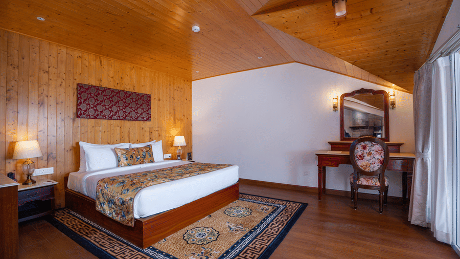 A bedroom at Summit Norbu Ghang - The Signature Collection, Gangtok, with a king size bed, bedside tables, rug, vanity table, and chair.