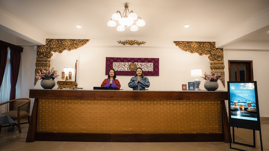 The reception area at Summit Norbu Ghang - The Signature Collection, Gangtok, with front desk, staff members, chandelier lighting, and display.
