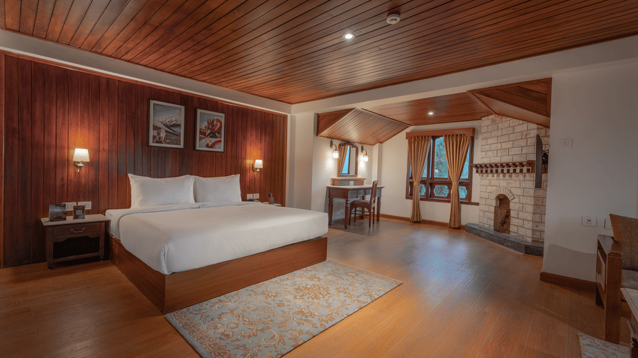 A bedroom at Summit Norbu Ghang - The Signature Collection, Gangtok, with a king size bed, bedside lamps, work desk, fireplace, and rug.