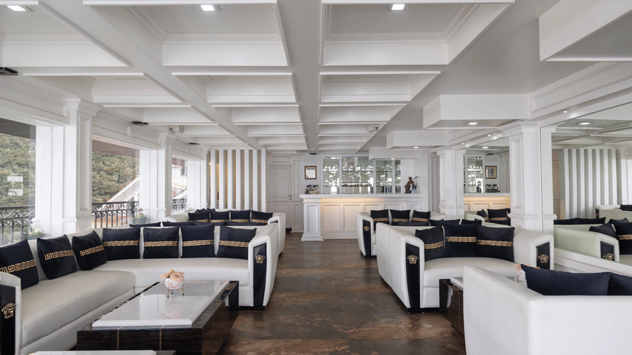 Indoor lounge area at The West Gate Posada By Summit, Darjeeling, featuring sofas with cushions arranged around coffee tables near a counter.