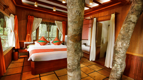 Room with a bed and tree trunks protruding out of the floor at Vythiri Resort, Wayanad