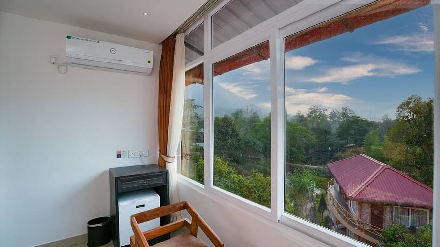 Deluxe room featuring large windows with a nature view, a spacious bed, air conditioning, wooden storage units, and a television at Summit Green Lake Tea Resort & Spa, Kaziranga1