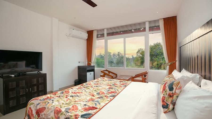 Deluxe room featuring large windows with a nature view, a spacious bed, air conditioning, wooden storage units, and a television at Summit Green Lake Tea Resort & Spa, Kaziranga2
