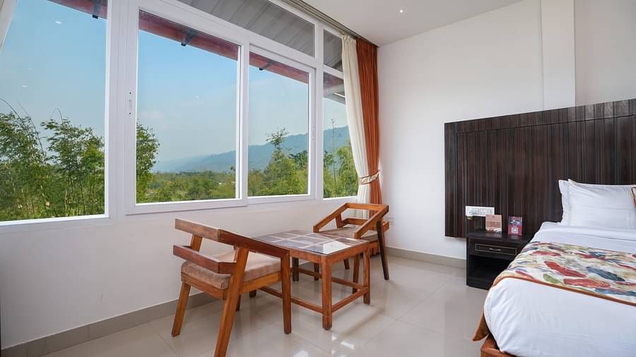 Deluxe room featuring large windows with a nature view, a spacious bed, air conditioning, wooden storage units, and a television at Summit Green Lake Tea Resort & Spa, Kaziranga3