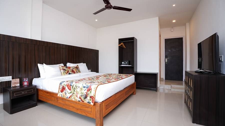 Deluxe room featuring large windows with a nature view, a spacious bed, air conditioning, wooden storage units, and a television at Summit Green Lake Tea Resort & Spa, Kaziranga6