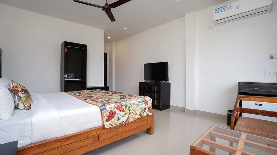 Deluxe room featuring large windows with a nature view, a spacious bed, air conditioning, wooden storage units, and a television at Summit Green Lake Tea Resort & Spa, Kaziranga7