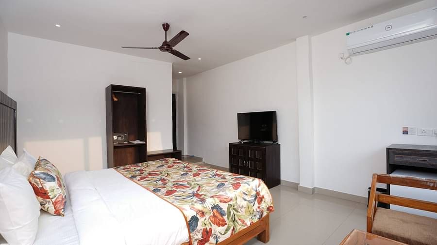 Deluxe room featuring large windows with a nature view, a spacious bed, air conditioning, wooden storage units, and a television at Summit Green Lake Tea Resort & Spa, Kaziranga8