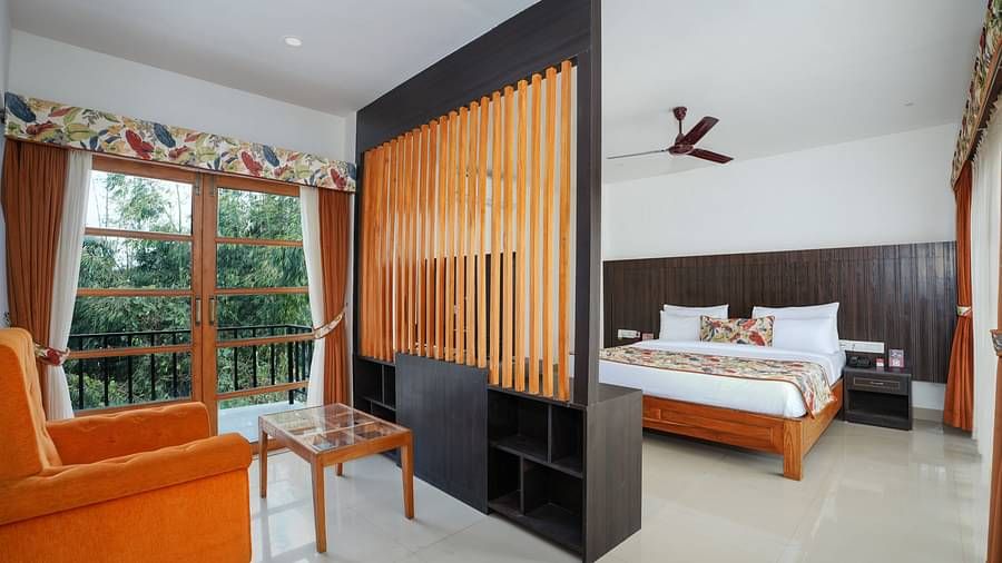 The suite with balcony includes a spacious bedroom area and living area with wooden furniture and a grille separating the two spaces at Summit Green Lake Tea Resort & Spa, Kaziranga