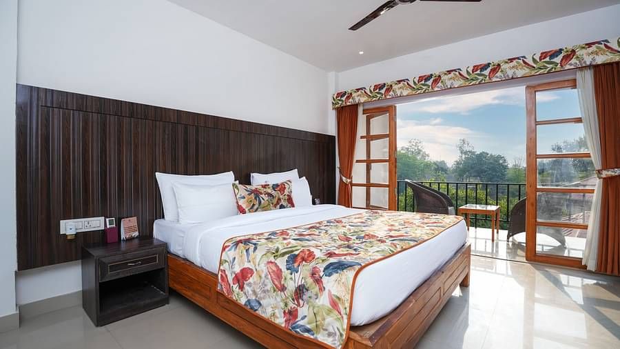 The suite with balcony offers a stunning nature view through large doors that open onto furniture and a glass table at Summit Green Lake Tea Resort & Spa, Kaziranga