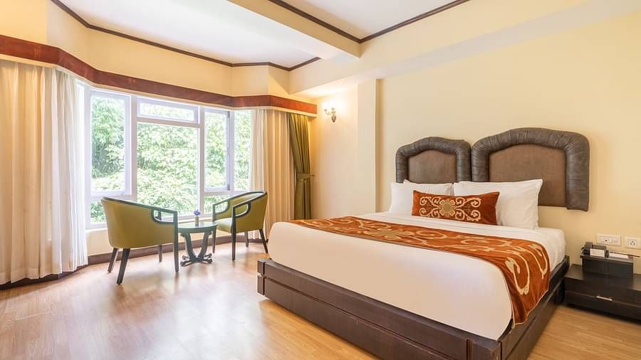 king size bed  with chairs near balcony of deluxe bed at Summit Lillium Hotel & Spa, Kalimpong