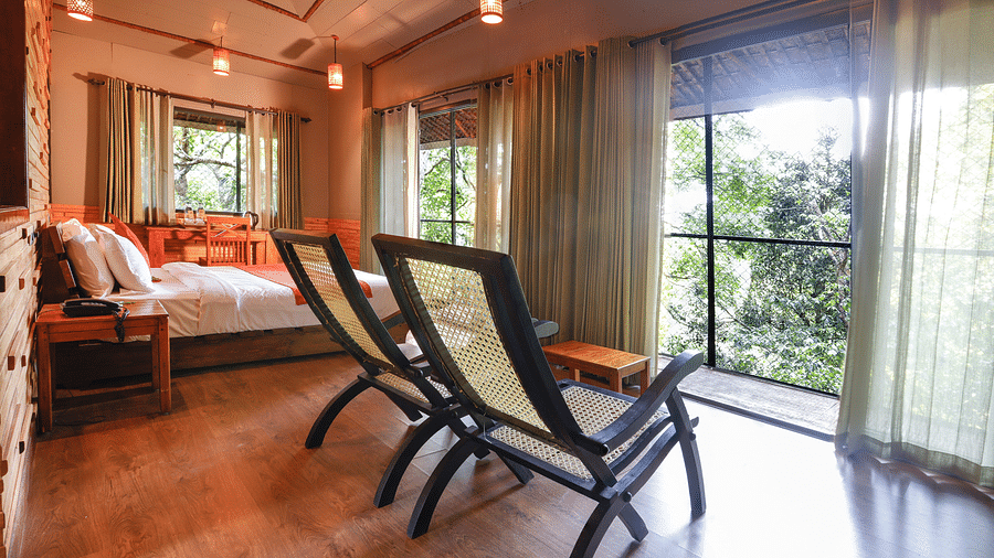 Two chairs and a bed in a room with balcony that offers forest views | Vythiri Resort. Wayanad