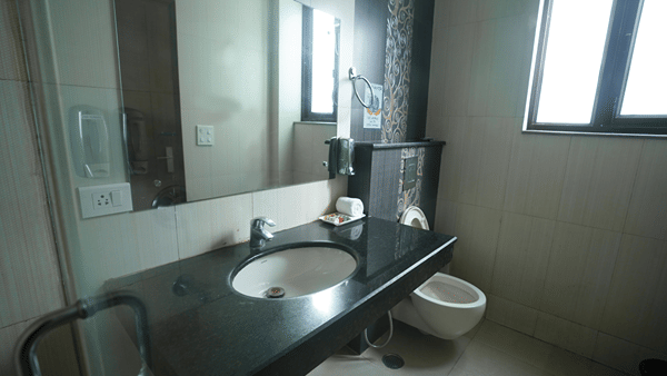 Bathroom with a granite vanity, sink, mirror, a rolled towel, a wall-hung toilet and a frosted window.