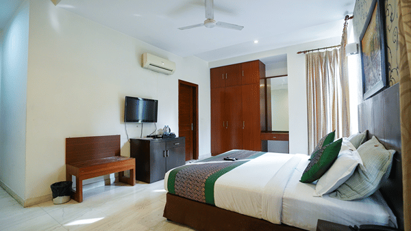 An image of a bedroom featuring a bed, a bedside table, a flat TV screen, a bench, a cabinet, and a wardrobe - Lime Tree Hotel, Iffco Chowk