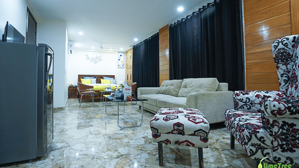 Studio suite at Lime Tree Hotel Near 32nd Avenue with a beige sofa, a wingback chair and a bed with yellow bedding.
