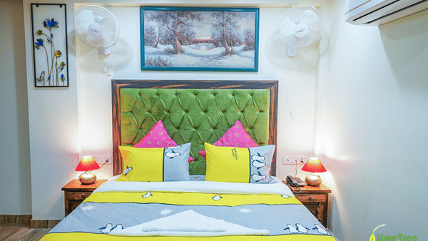 Bedroom at Lime Tree Hotel Near 32nd Avenue with a green tufted headboard, a snowy forest painting and red table lamps.