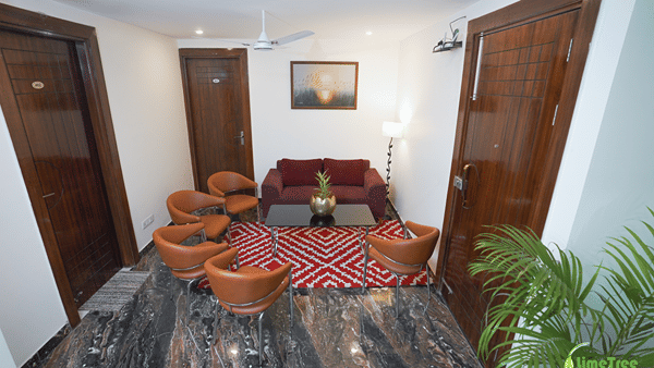 Lounge at Lime Tree Hotel Near 32nd Avenue with a maroon sofa, 4 tan leather chairs, a glass table and a red rug.