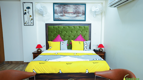 Double bed with a green tufted headboard, yellow bedding and pink cushions.