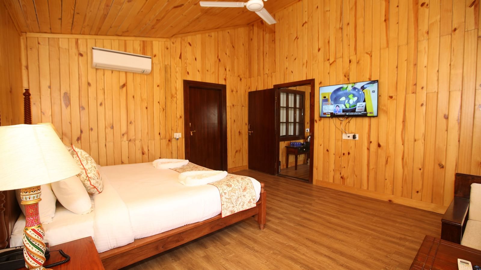 Spacious Kashmir Cottage Villa's Pool room with a king-sized bed, wooden flooring, and a wall-mounted TV at Aanandam Resort & Spa