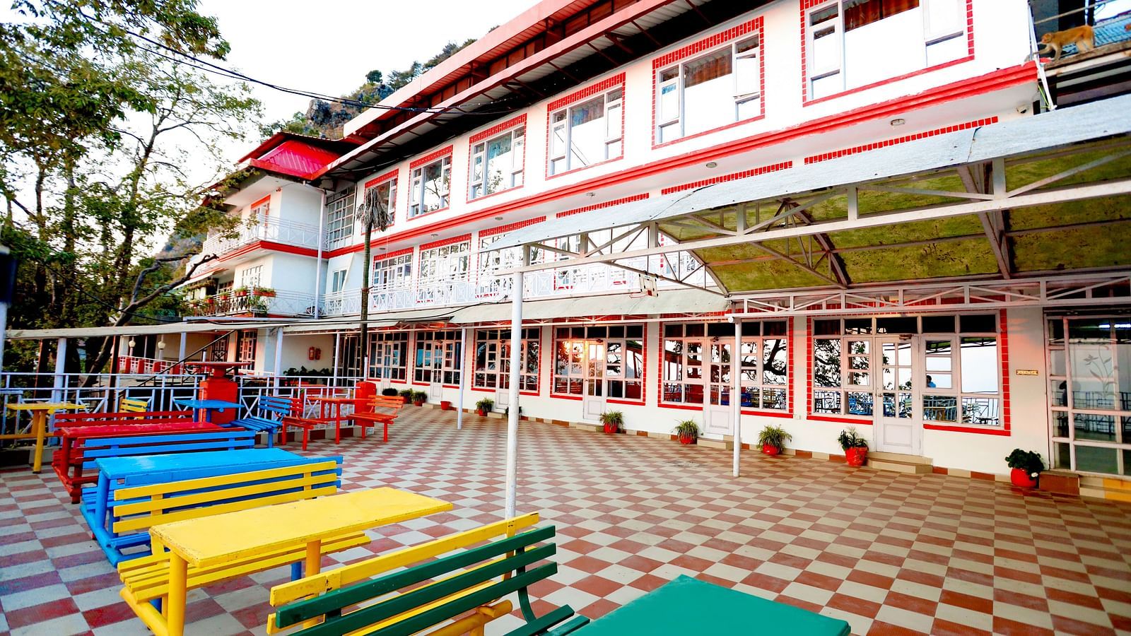Facade of Amara Hill Queen, Mussoorie with a seating area in front with benches and chairs.