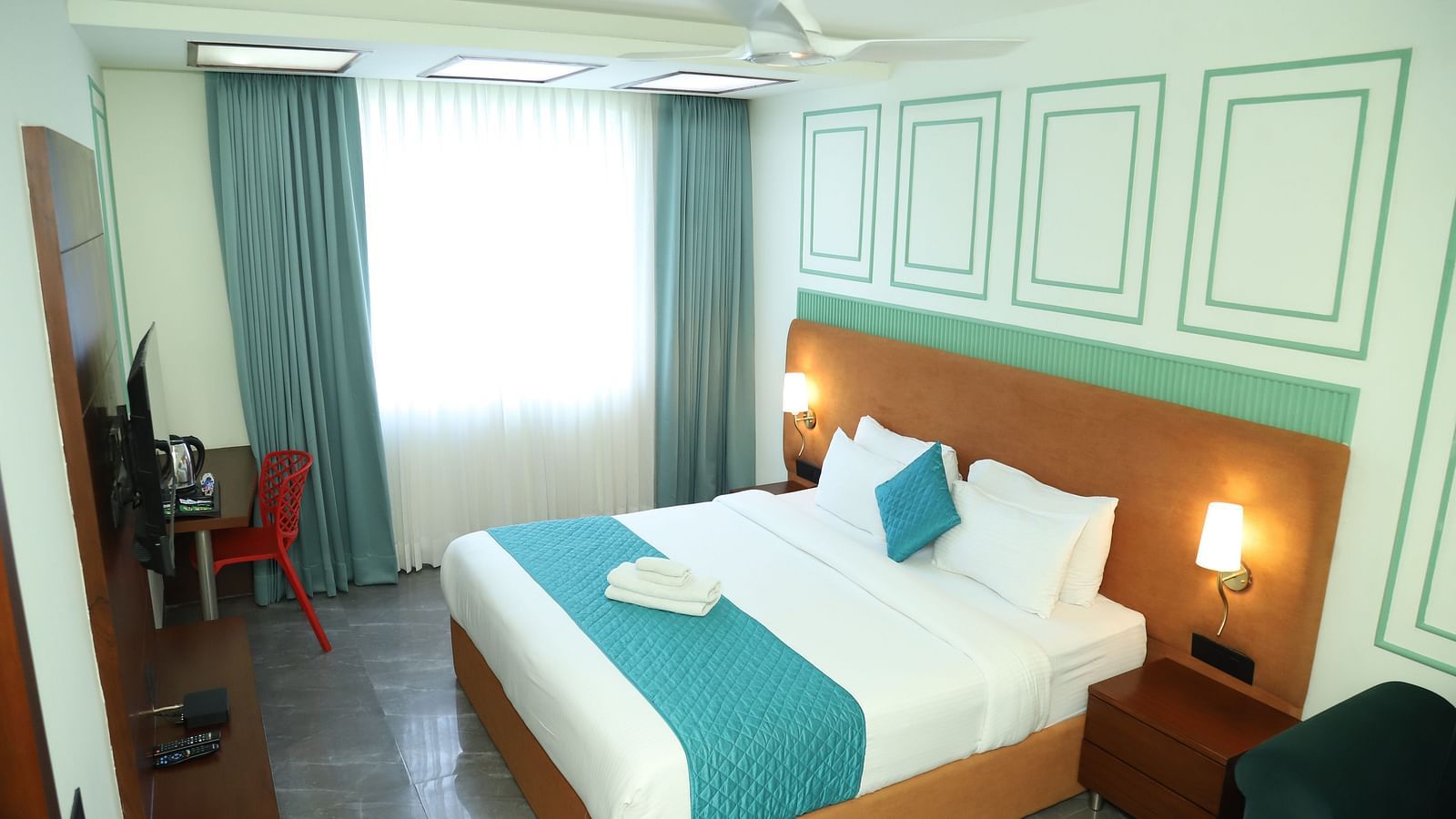 A comfortable room includes a double bed with a turquoise accent and wooden furniture - Asian Suites IFFCO Metro, Gurgaon
