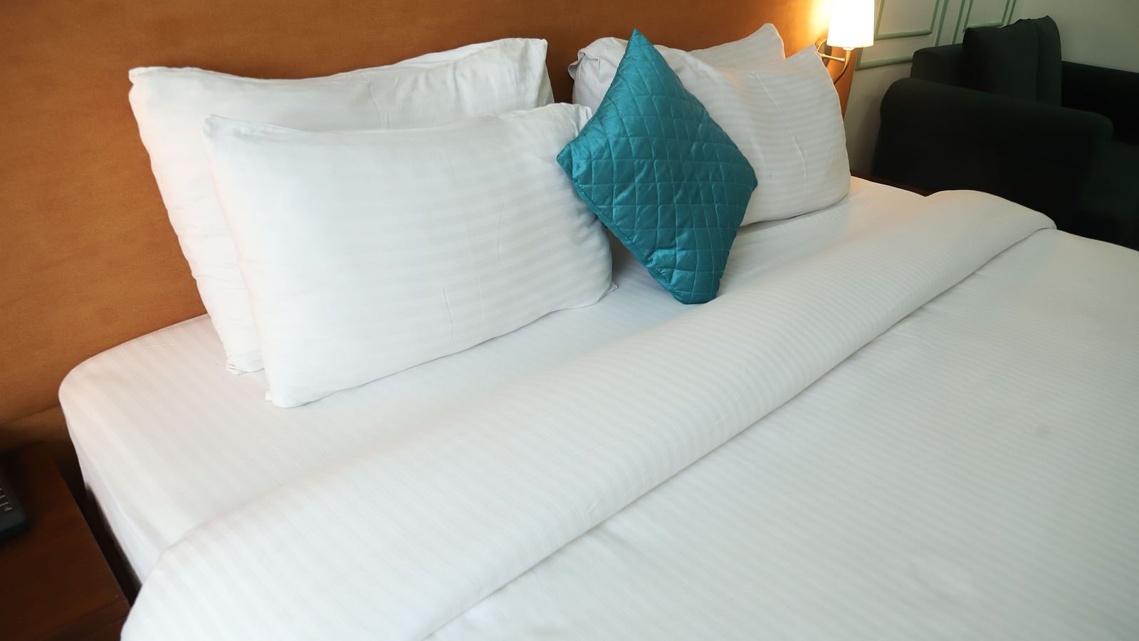 A close-up of a bed with white linens, several white pillows, and a single teal cushion - Asian Suites IFFCO Metro, Gurgaon
