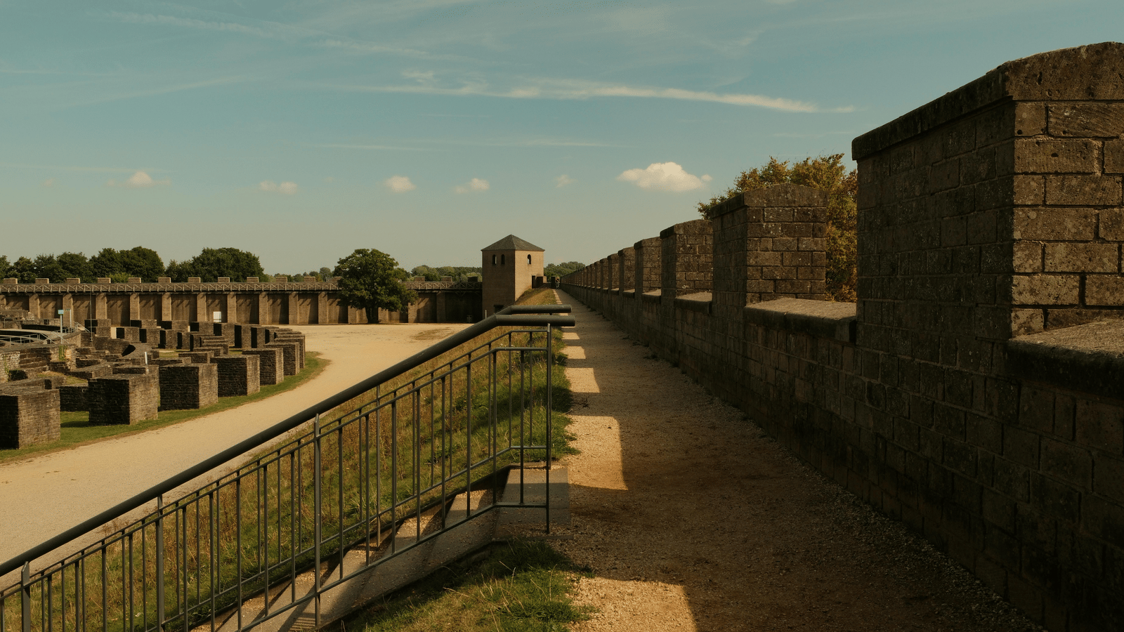 A historical stone rampart or defensive wall extending into the distance under a sunny blue sky, with crenellations along the top.