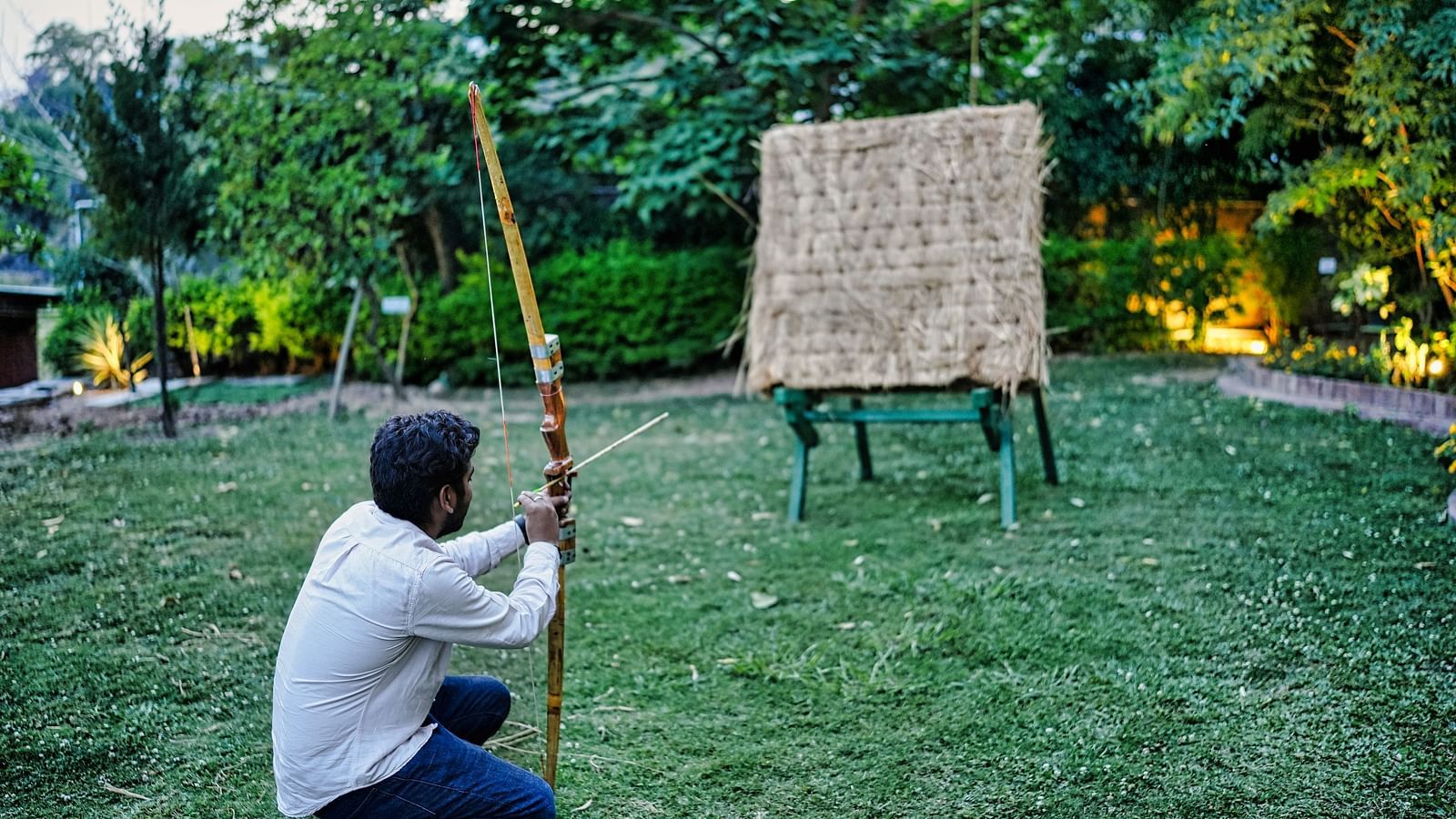 An image of a man trying out archery, aiming at the target, captured from back in a day light.