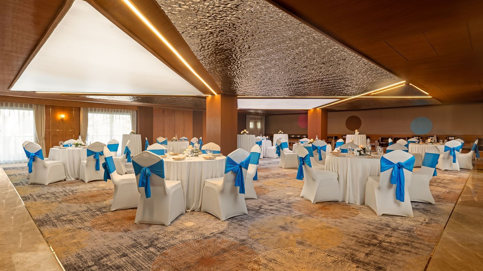 Indoor wedding ceremony with blue-clad performers, high ceilings, and warm lighting, capturing a cultural ritual in progress.