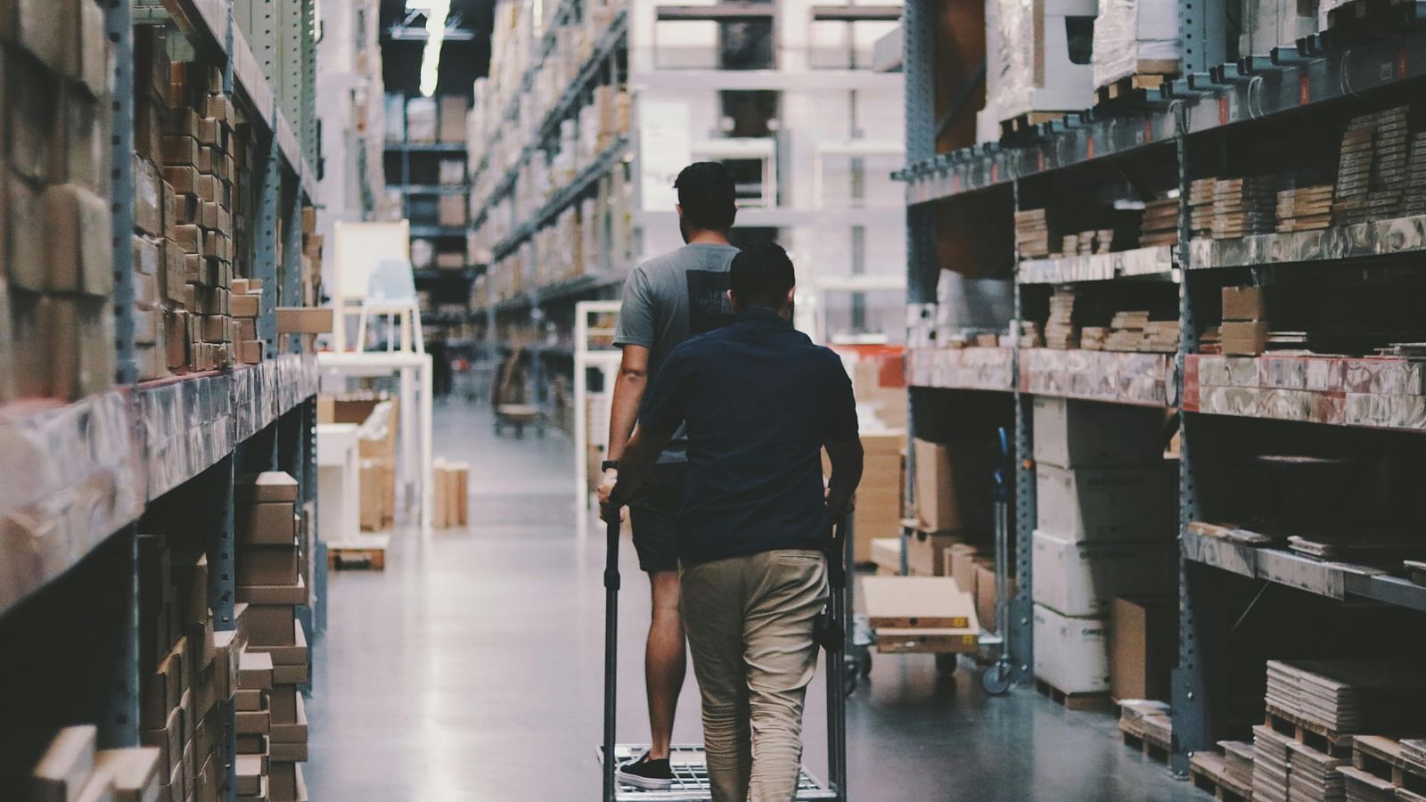 Person walking with a trolley bag through a warehouse aisle