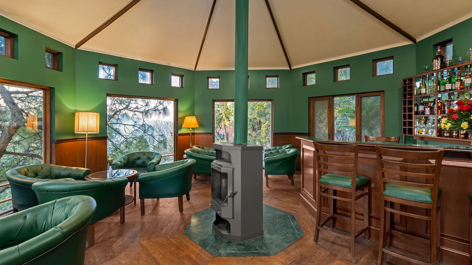 A bar featuring a wooden and green decor, with high chairs and sofas arranged comfortably with warm light lamps -  Baikunth resort, kasauli 