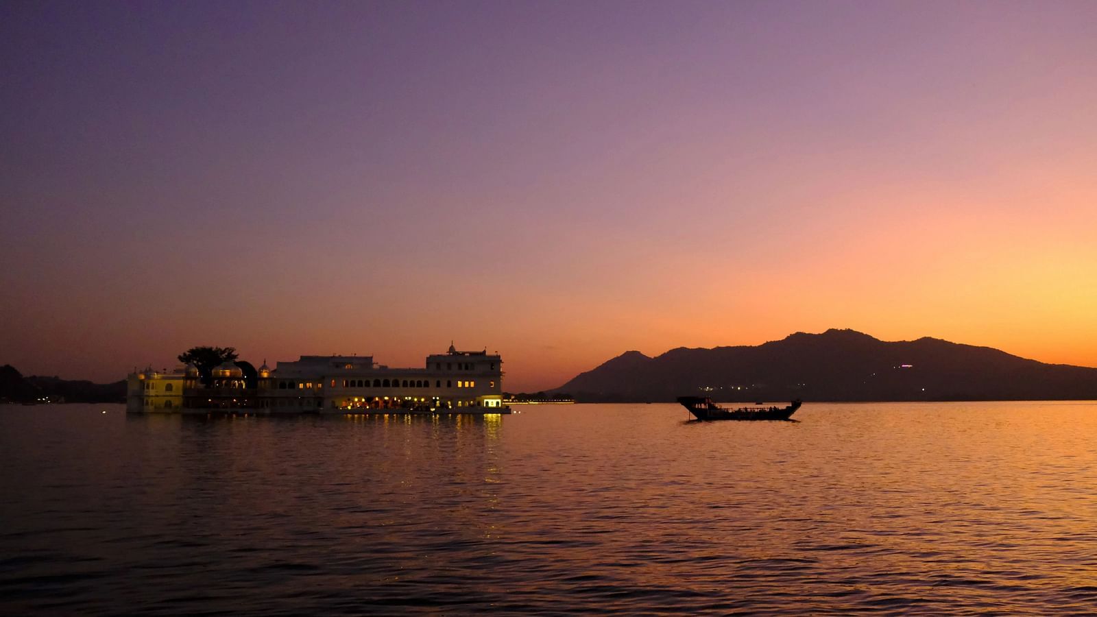 Sunset over a lake with a boat and hills in the distance.