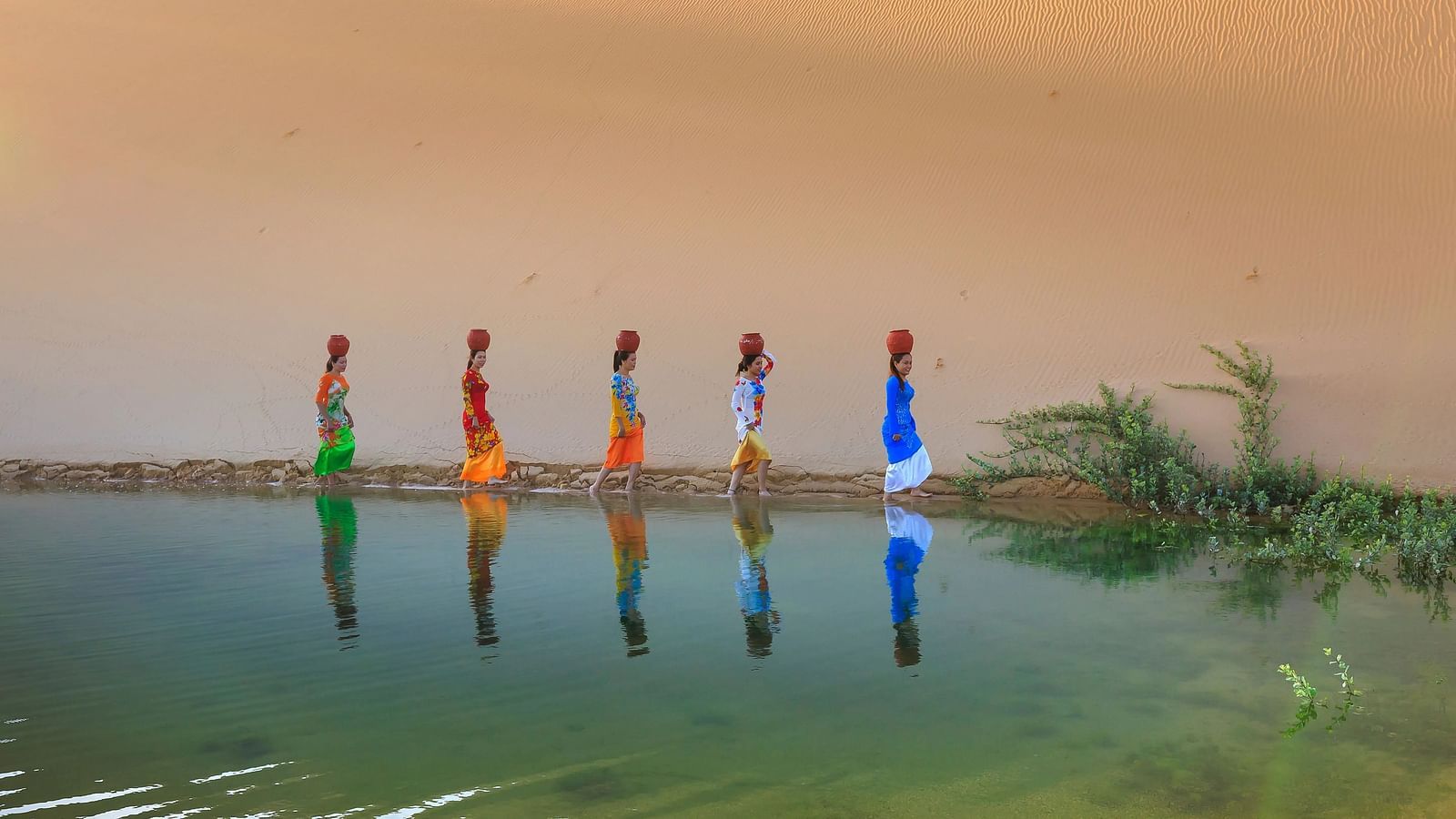  Silhouetted figures stand in shallow water at sunset.